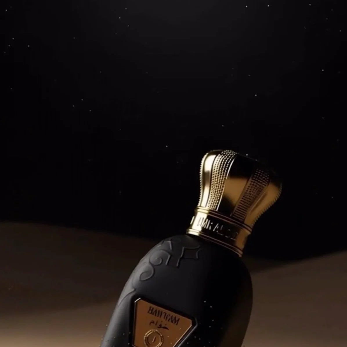 Hawwam Perfume by Jamr Al Oud, black bottle with a gold cap on sand under a crescent moon.