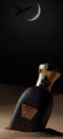 Hawwam Perfume by Jamr Al Oud, black bottle with a gold cap on sand under a crescent moon.